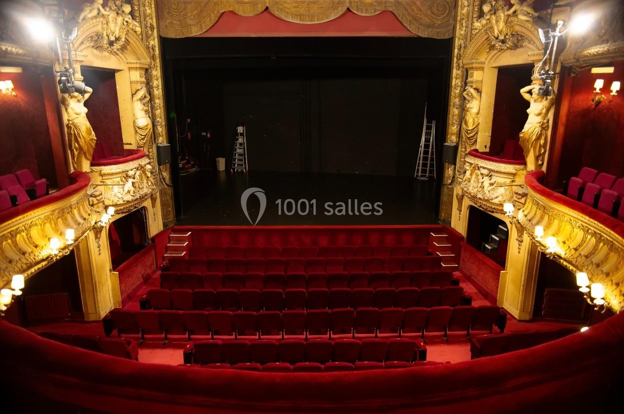 Salle de théâtre vide avec sièges rouges, balcons ornés et scène sombre en arrière-plan.