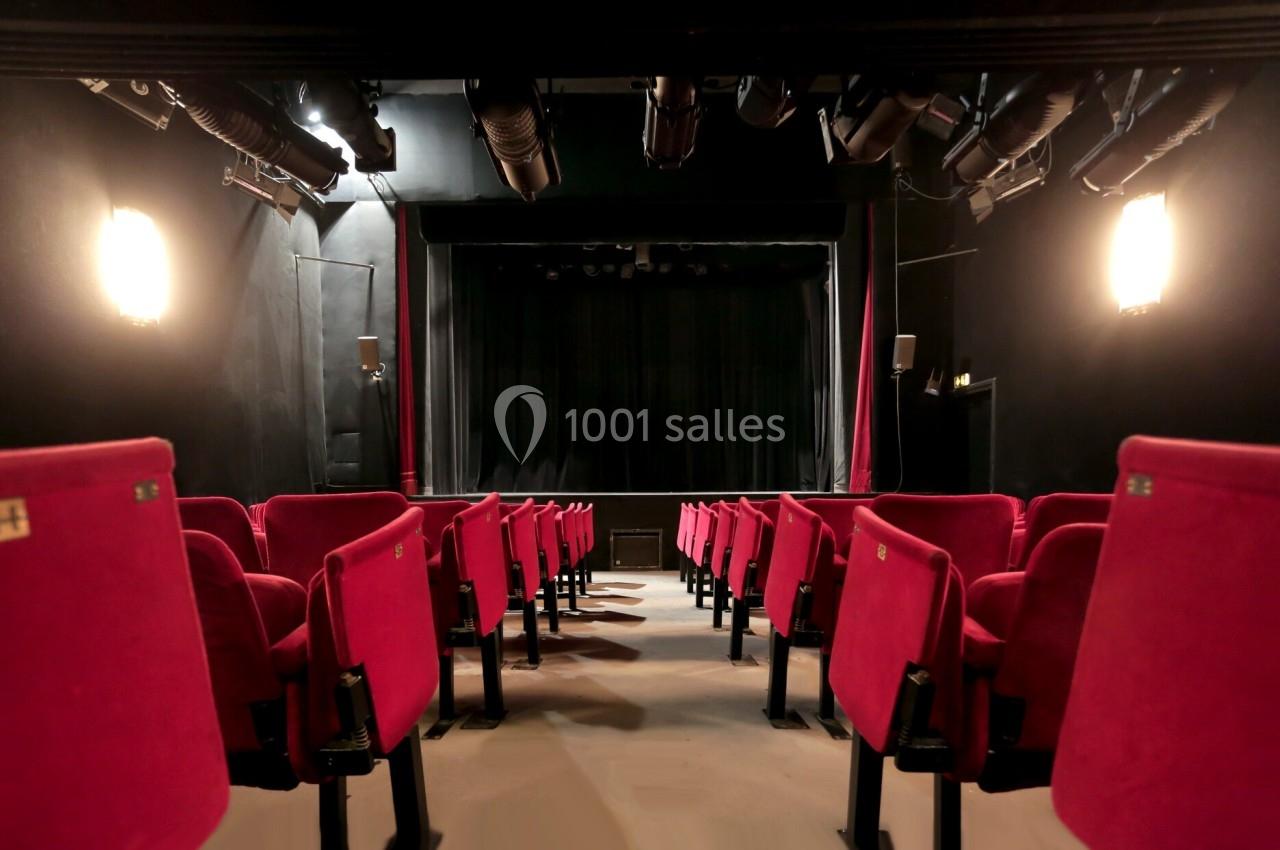 Salle de théâtre vide avec des rangées de sièges rouges et une scène sombre en arrière-plan.
