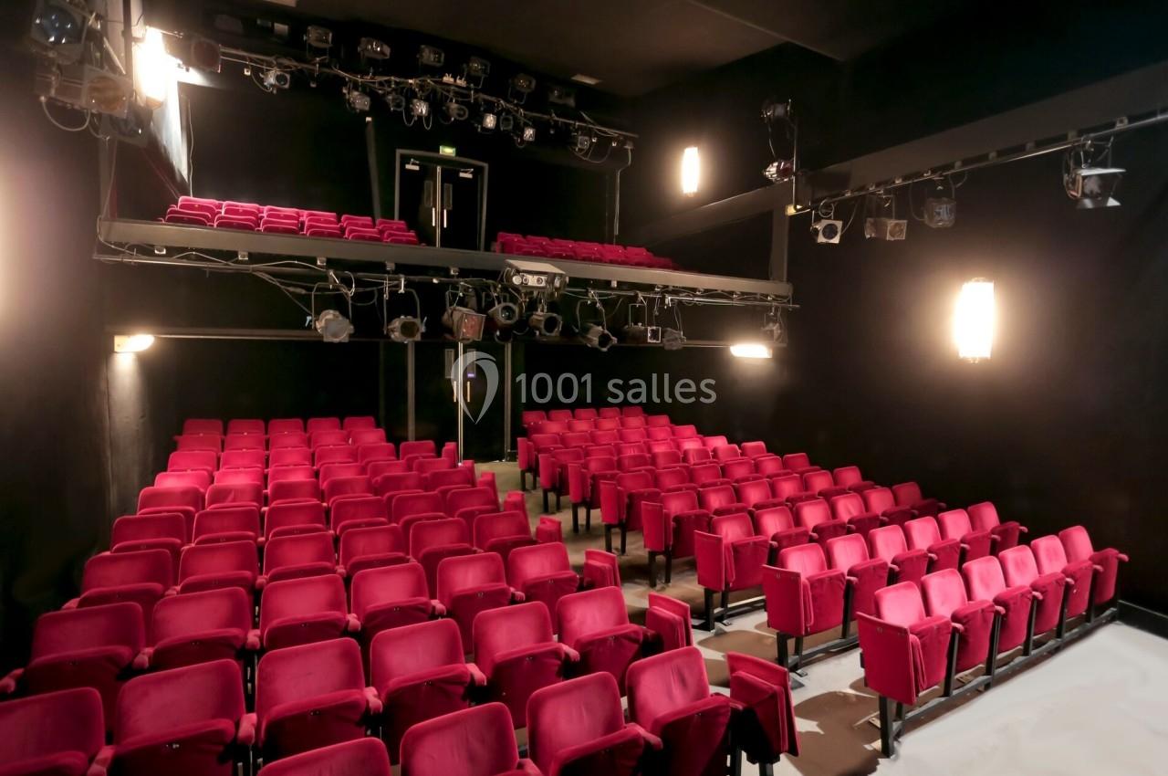 Salle de théâtre avec des rangées de sièges rouges, un balcon supérieur et des projecteurs suspendus.
