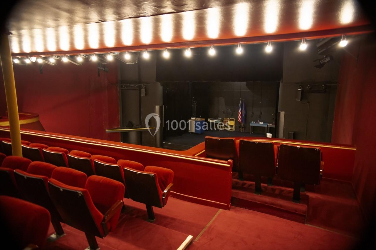 Salle de théâtre vide avec sièges rouges, scène sombre en arrière-plan et drapeau américain visible.