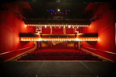 Hall d'entrée d'un théâtre avec affiches de spectacles sur les murs et comptoir d'accueil à gauche.