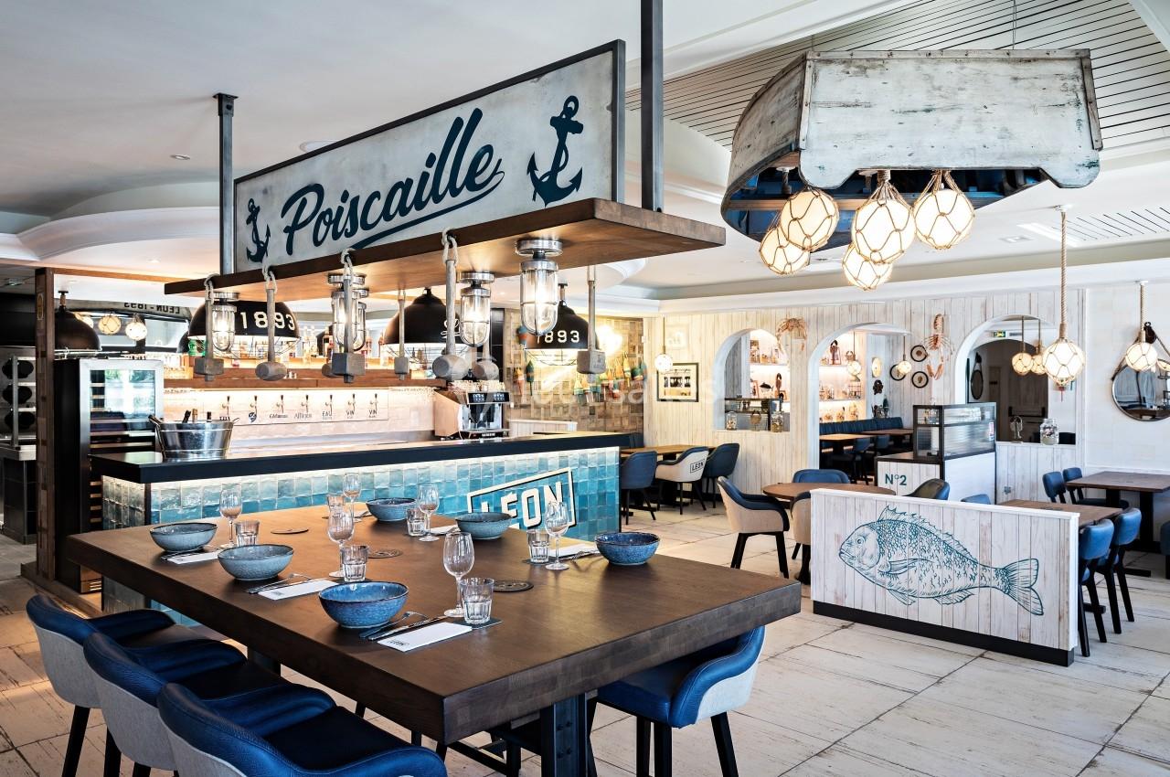 Salle de restaurant au style marin avec décorations nautiques, tables dressées et comptoir en arrière-plan.