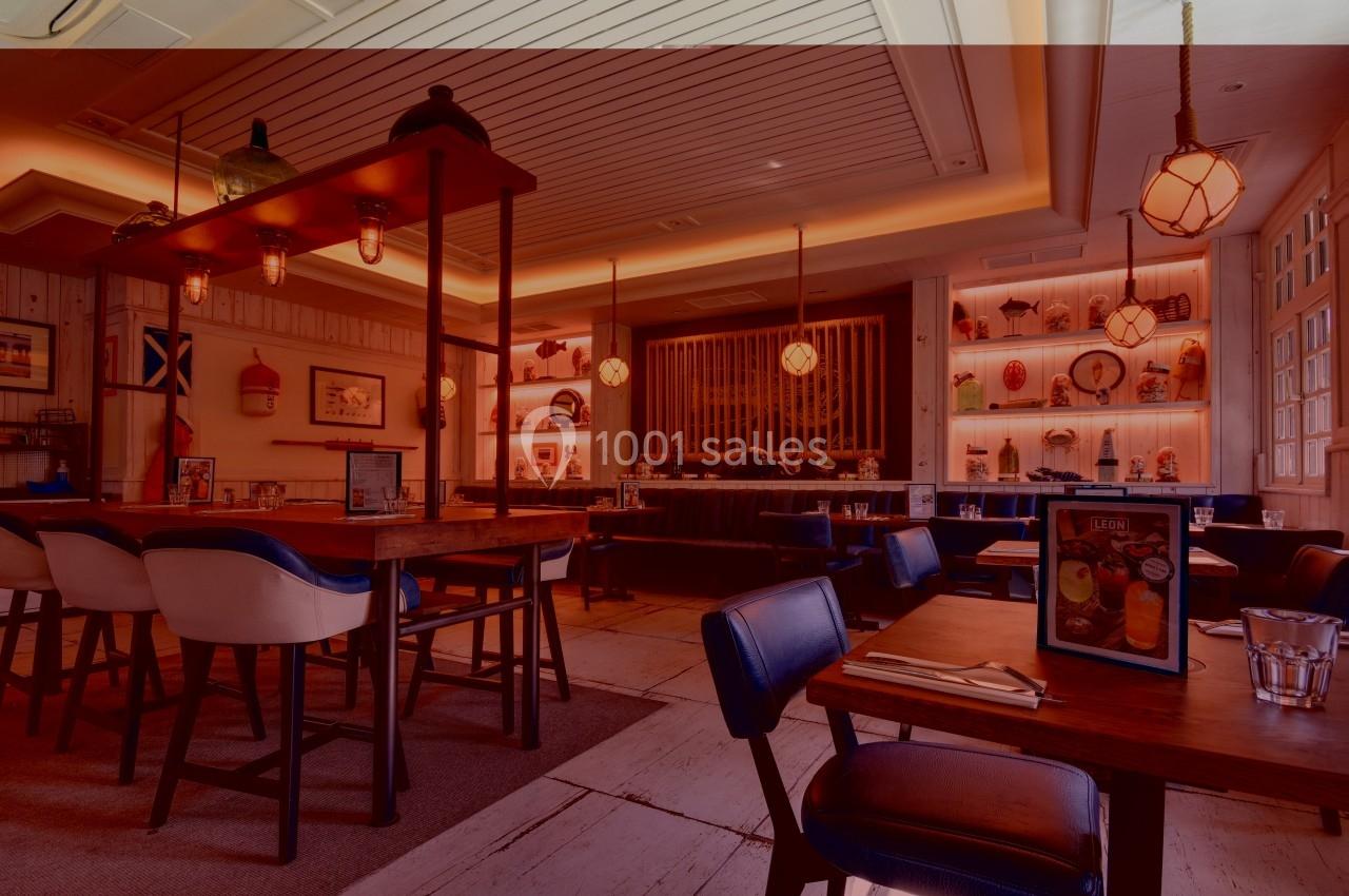 Salle de restaurant chaleureuse avec tables en bois, chaises rembourrées et éclairage tamisé.