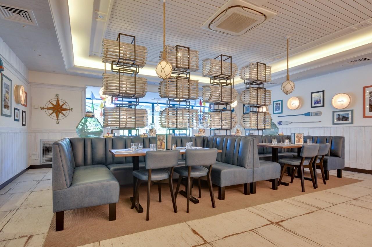 Salle de restaurant lumineuse avec banquettes bleues, tables dressées et décor marin aux murs.