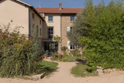 Façade en pierre d'une maison à trois étages avec volets blancs, jardin arboré et allée gravillonnée au premier plan.