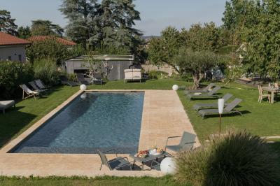 Façade en pierre d'une maison à trois étages avec volets blancs, jardin arboré et allée gravillonnée au premier plan.