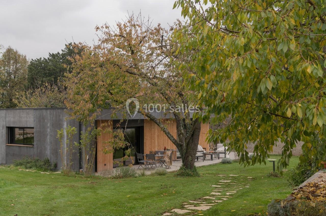 Maison contemporaine en bois et béton entourée d'un jardin verdoyant avec un arbre au premier plan.