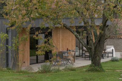Façade en pierre d'une maison à trois étages avec volets blancs, jardin arboré et allée gravillonnée au premier plan.