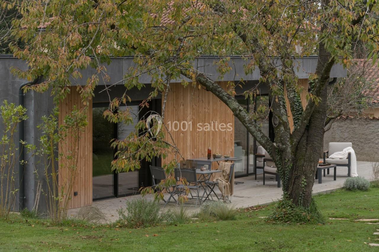 Terrasse en bois aménagée avec table et chaises, entourée de verdure et d'un arbre aux feuilles automnales.