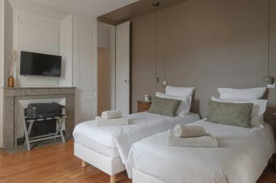 Façade en pierre d'une maison à trois étages avec volets blancs, jardin arboré et allée gravillonnée au premier plan.