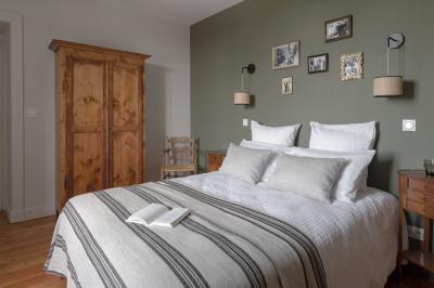 Façade en pierre d'une maison à trois étages avec volets blancs, jardin arboré et allée gravillonnée au premier plan.