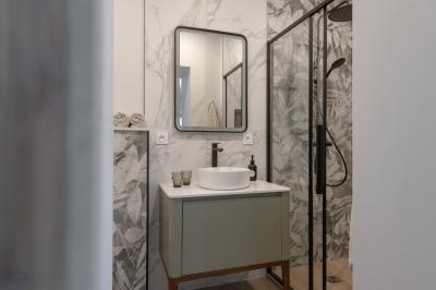 Façade en pierre d'une maison à trois étages avec volets blancs, jardin arboré et allée gravillonnée au premier plan.