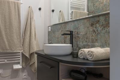 Façade en pierre d'une maison à trois étages avec volets blancs, jardin arboré et allée gravillonnée au premier plan.