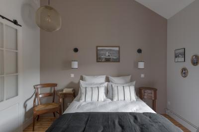 Façade en pierre d'une maison à trois étages avec volets blancs, jardin arboré et allée gravillonnée au premier plan.