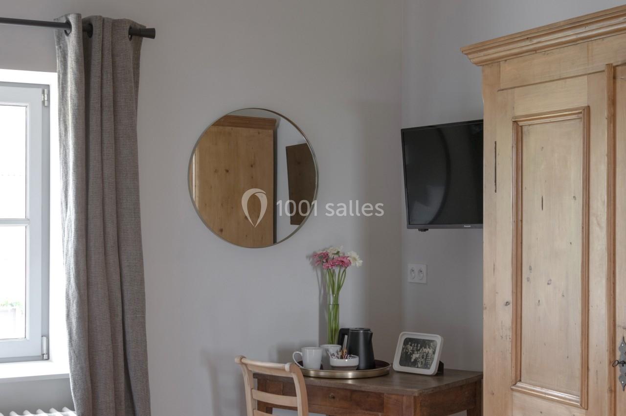 Coin bureau avec table en bois, chaise, miroir rond, télévision murale, armoire en bois et fenêtre avec rideaux gris.