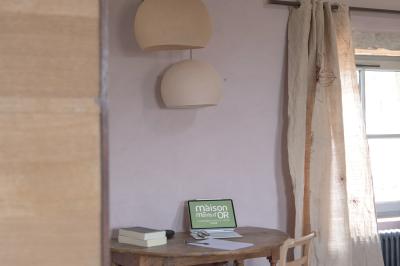 Façade en pierre d'une maison à trois étages avec volets blancs, jardin arboré et allée gravillonnée au premier plan.