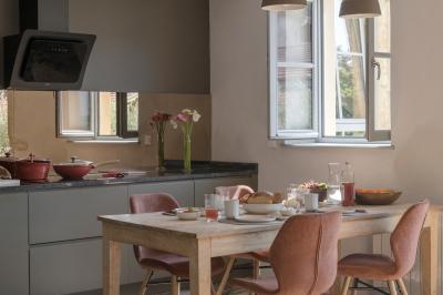 Façade en pierre d'une maison à trois étages avec volets blancs, jardin arboré et allée gravillonnée au premier plan.