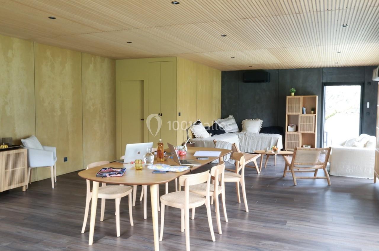 Salle de séjour lumineuse avec table en bois, chaises, canapé, étagères et décoration minimaliste.