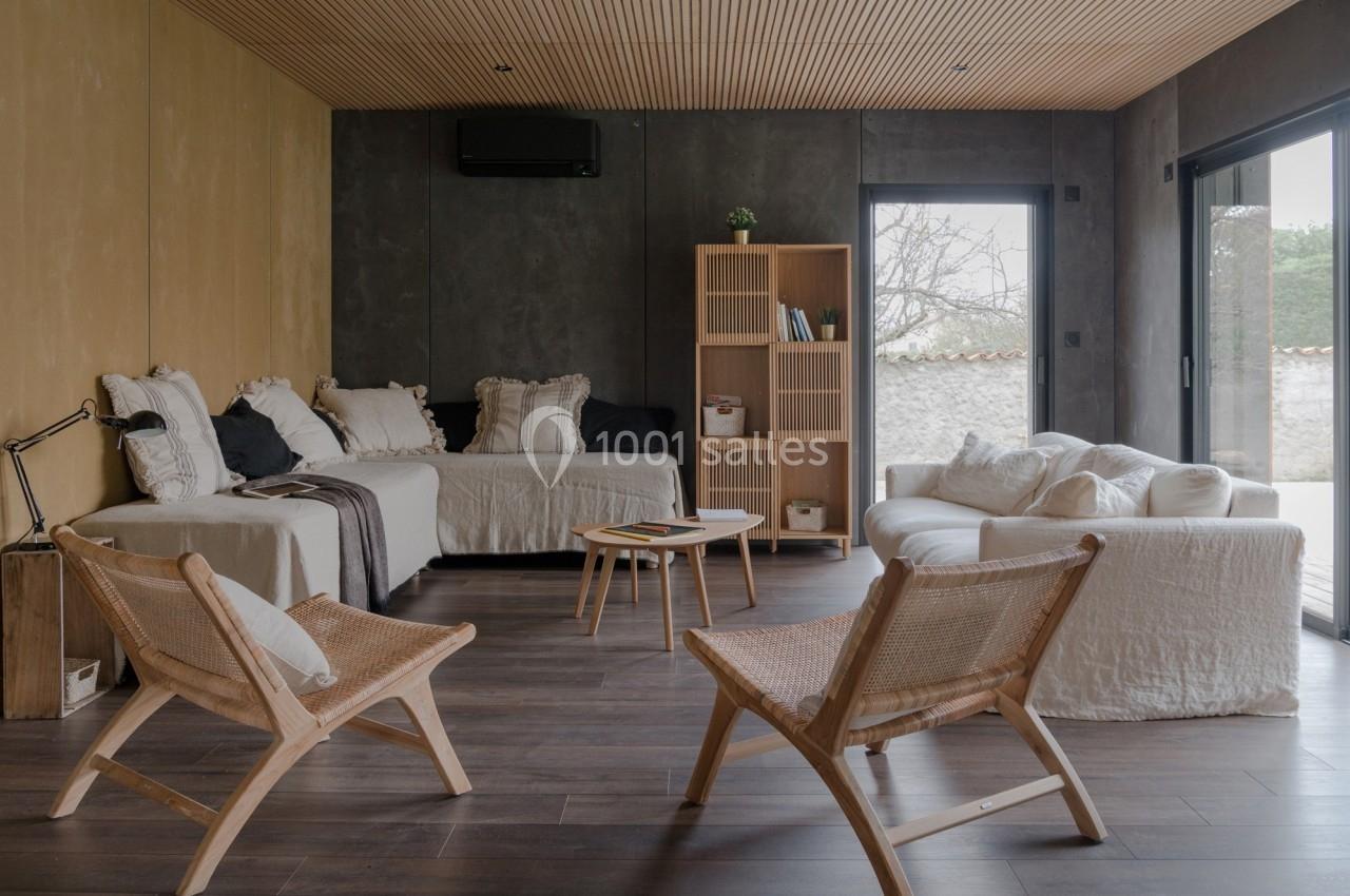 Salon moderne avec canapé beige, fauteuils en bois, bibliothèque, table basse et grandes baies vitrées donnant sur l…