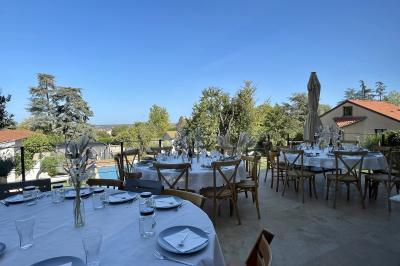 Façade en pierre d'une maison à trois étages avec volets blancs, jardin arboré et allée gravillonnée au premier plan.
