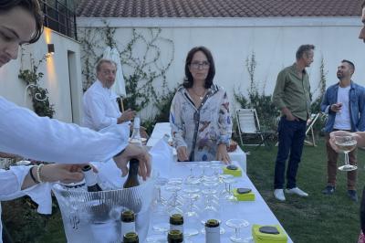 Façade en pierre d'une maison à trois étages avec volets blancs, jardin arboré et allée gravillonnée au premier plan.