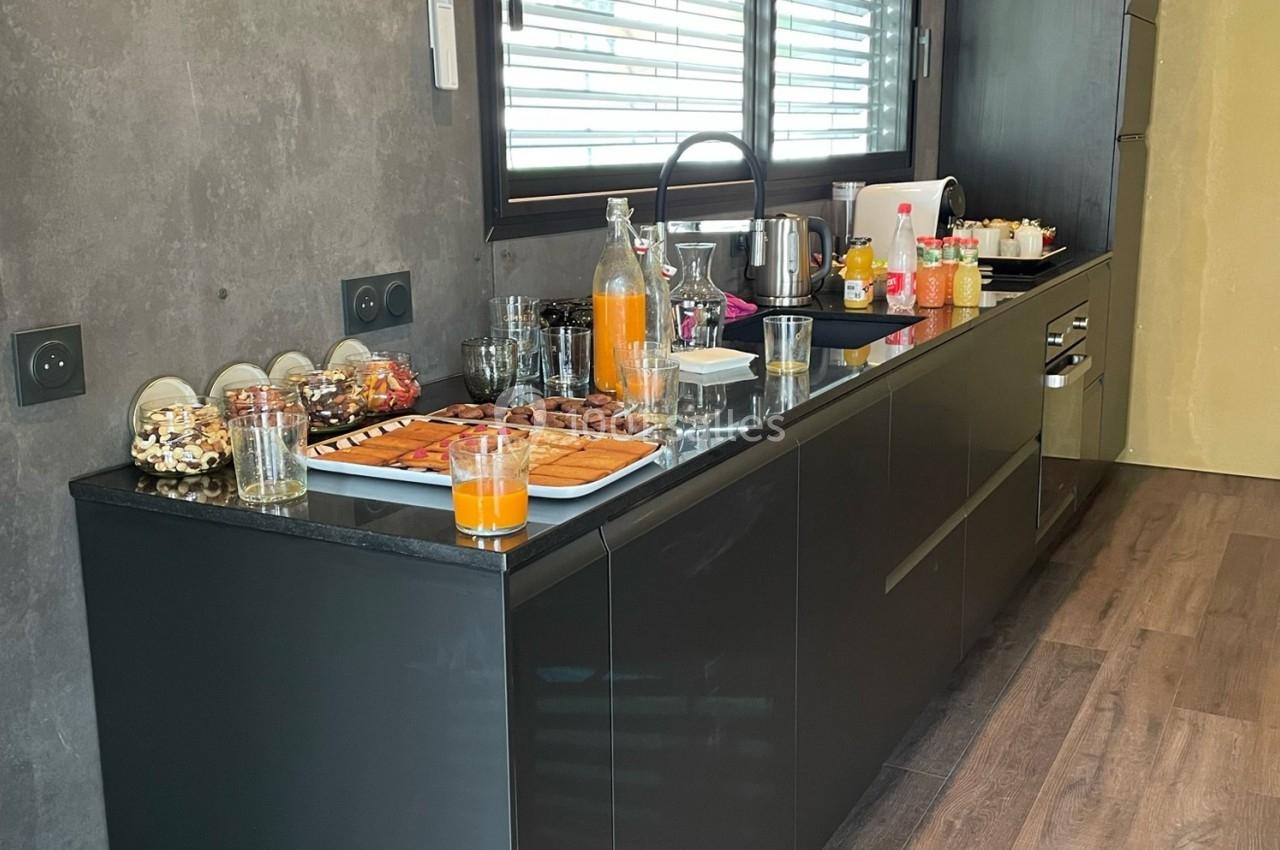 Buffet de petit-déjeuner avec viennoiseries, jus de fruits et boissons disposés sur un plan de travail moderne.