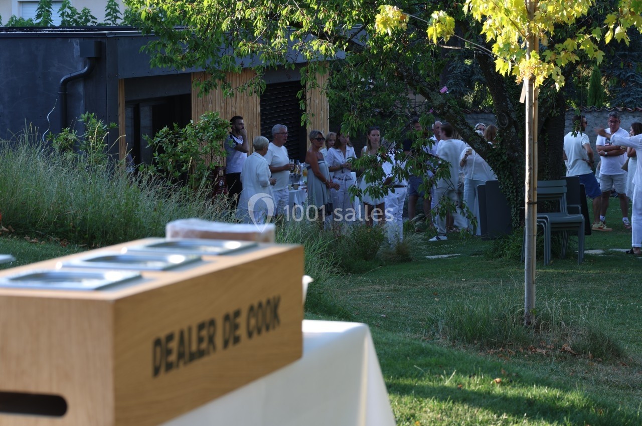 Groupe de personnes en tenue blanche rassemblées dans un jardin, avec une boîte en bois marquée ’Dealer de Cook’ au premier…