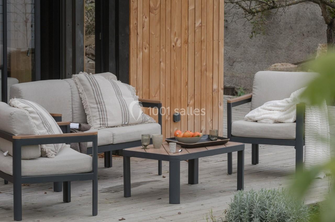 Salon de jardin avec canapés beiges et table basse, installé sur une terrasse en bois près d'un mur en bois clair.