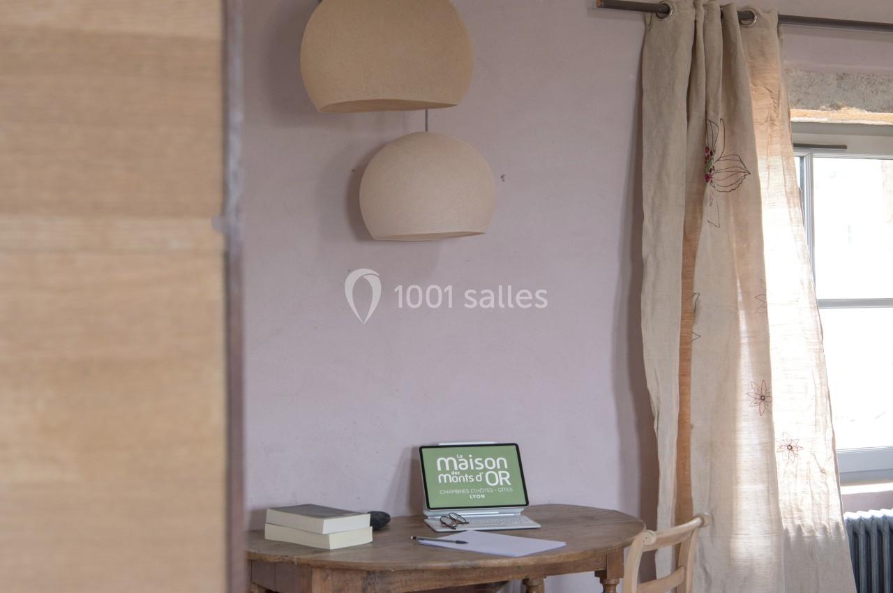 Bureau en bois avec chaise noire, lampe suspendue, rideaux en lin et ordinateur portable sur une table près d'une fenêtre.