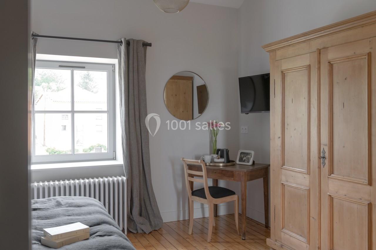 Chambre lumineuse avec un lit, une armoire en bois, un bureau près d'une fenêtre et un miroir rond au mur.
