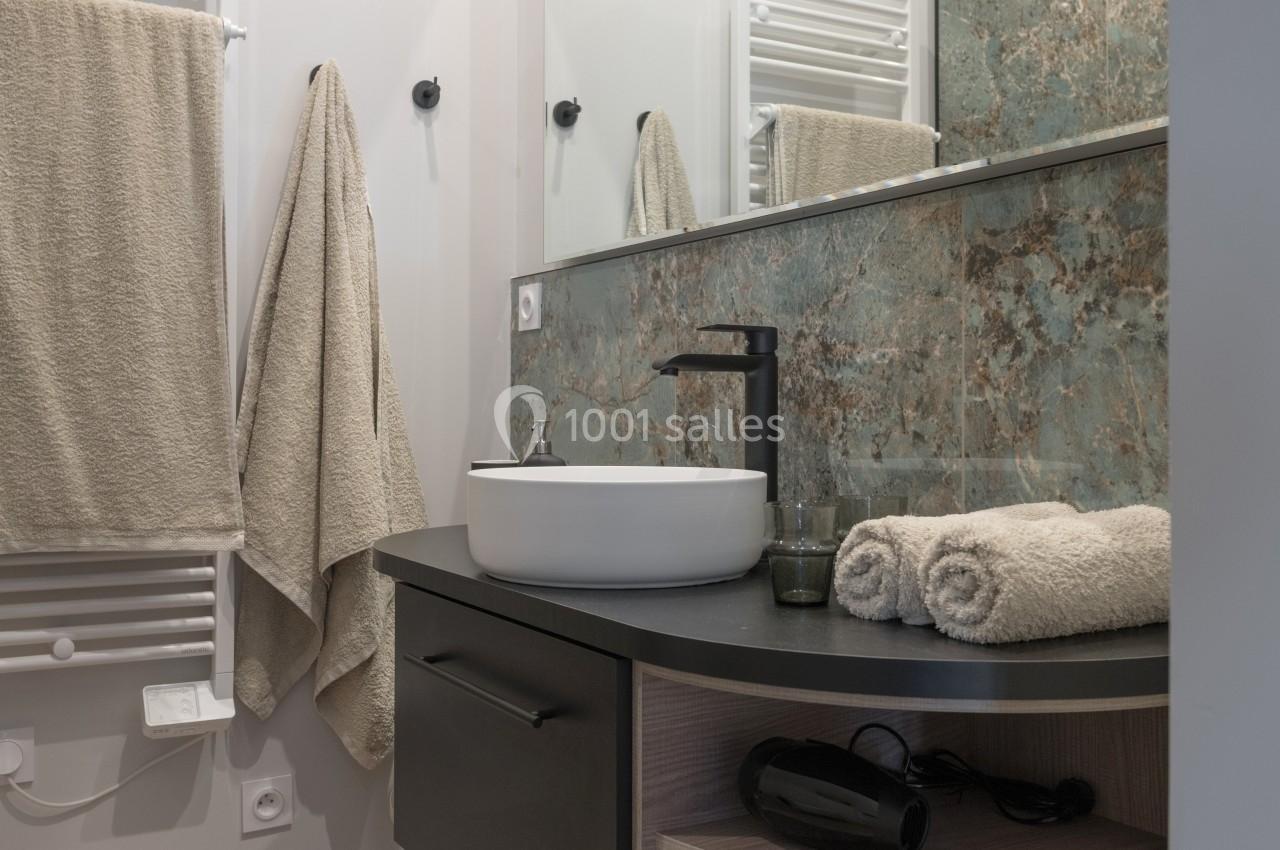 Salle de bain moderne avec lavabo sur meuble noir, miroir, serviettes beiges et mur partiellement carrelé.