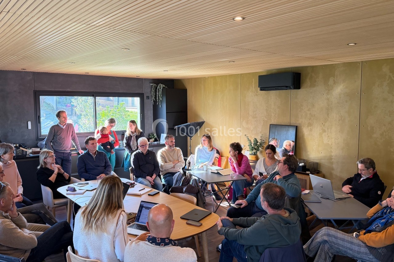 Un groupe de personnes assises autour de tables en réunion dans une salle lumineuse avec un plafond en bois.