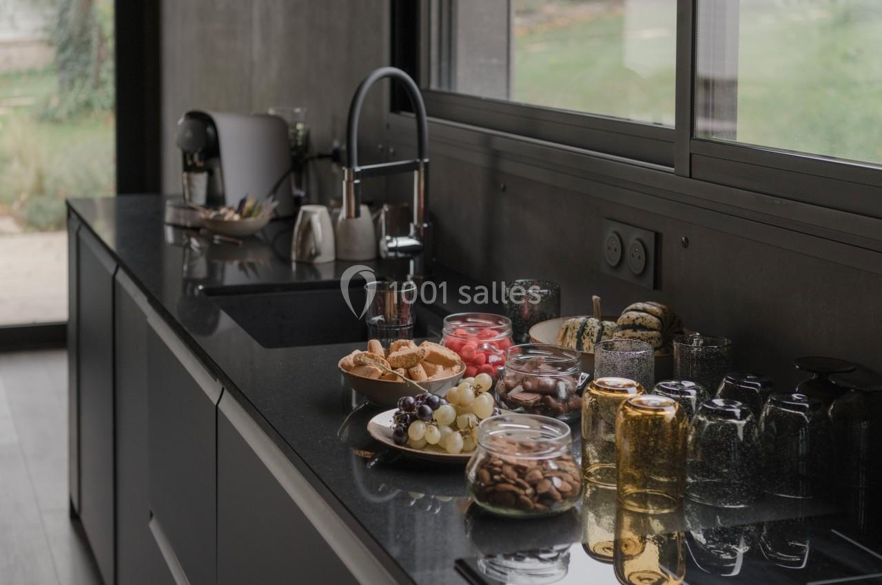 Plan de travail de cuisine moderne avec évier, fruits, biscuits et bocaux en verre, près d'une fenêtre donnant sur un jardin.