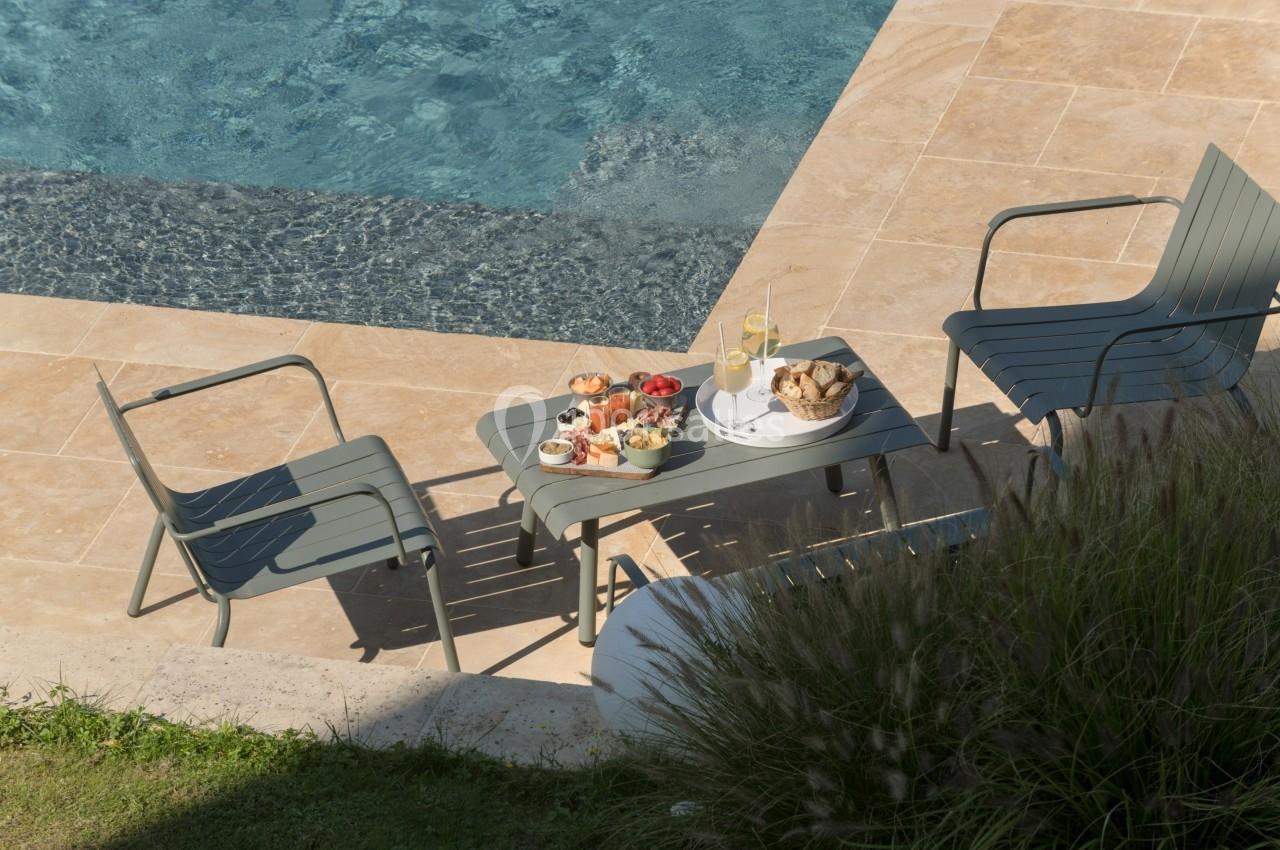 Table basse avec des collations et boissons entourée de deux chaises près d'une piscine sur une terrasse en pierre.