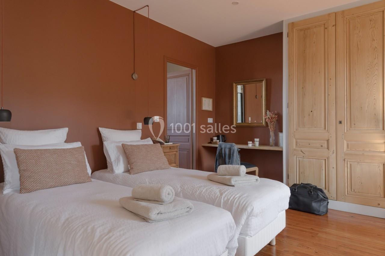 Chambre avec deux lits simples, murs couleur terracotta, meubles en bois clair et lumière naturelle.