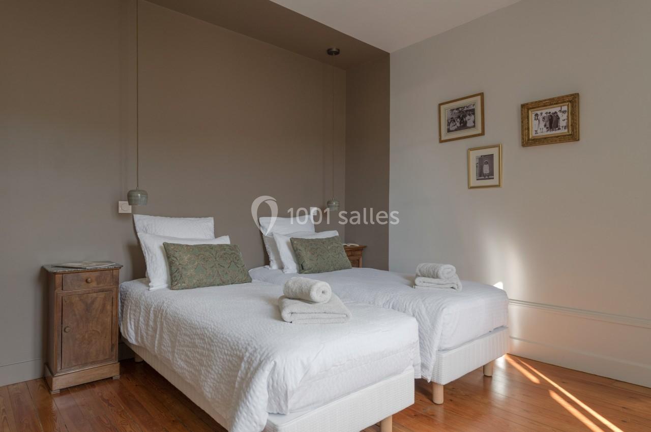 Deux lits simples avec linge blanc, coussins décoratifs et chevets en bois, dans une chambre aux murs beige.