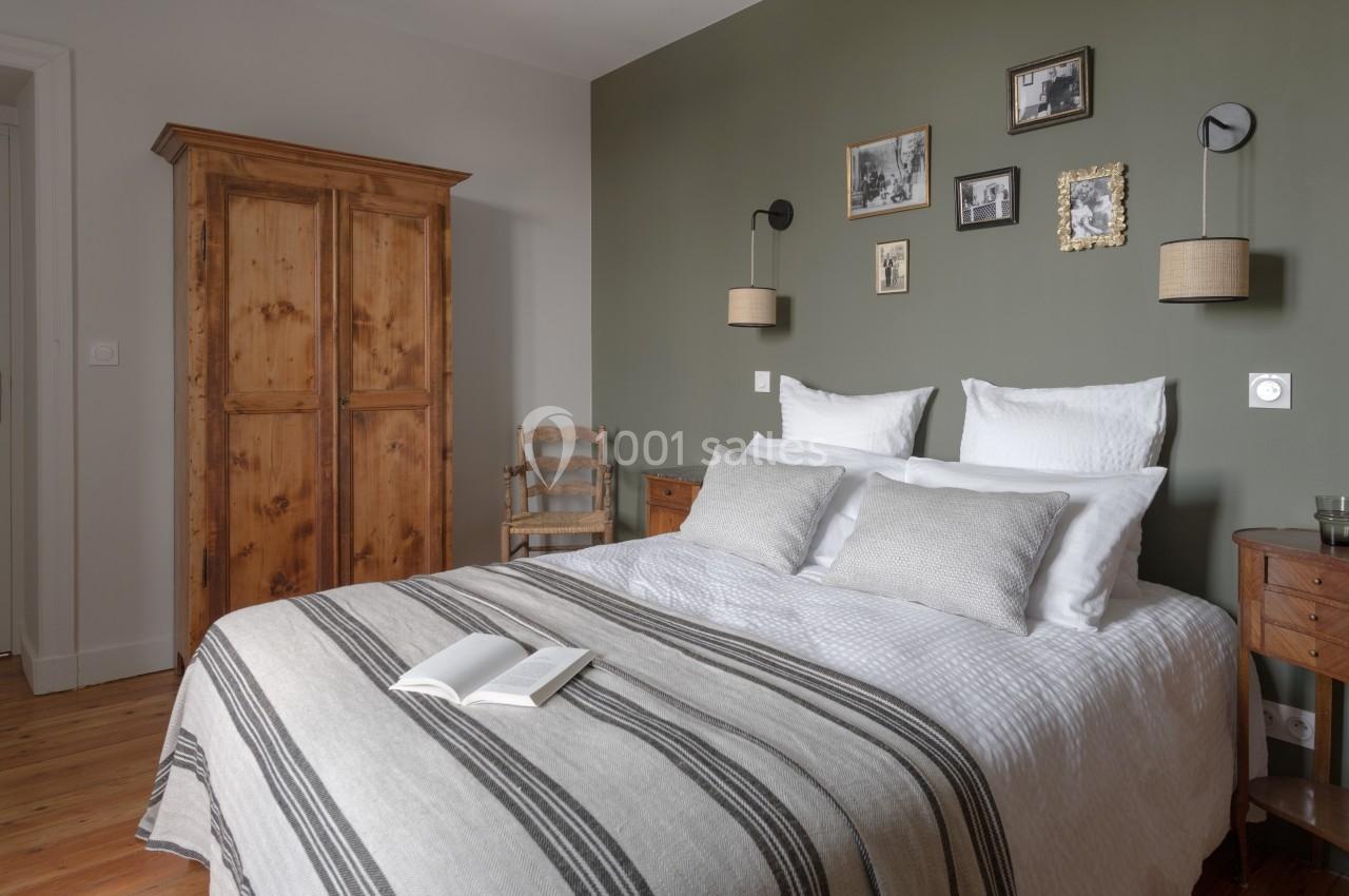 Chambre avec lit double, armoire en bois, mur vert décoré de cadres, et lumière naturelle.