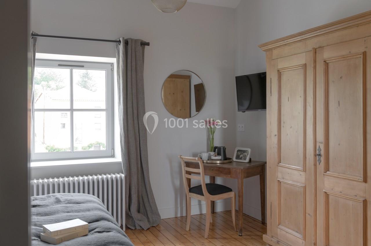 Chambre lumineuse avec un lit, une armoire en bois, un bureau, une chaise, un miroir rond et une fenêtre donnant sur l…