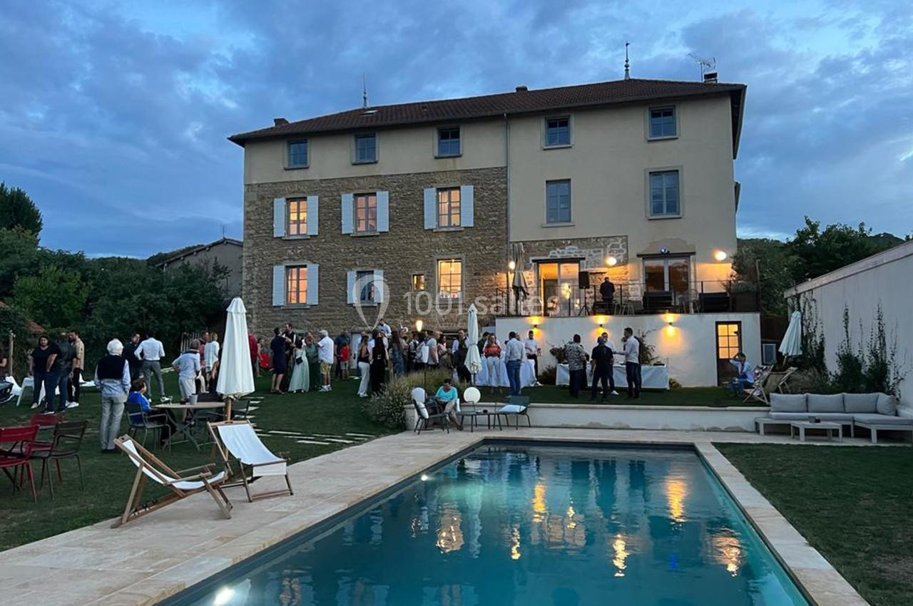 Groupe de personnes rassemblées dans le jardin d'une grande maison en soirée, avec une piscine au premier plan.