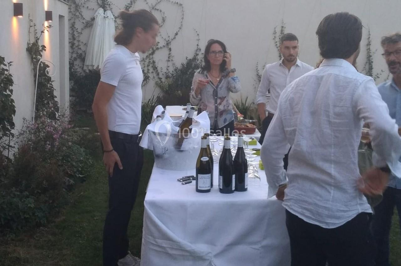 Des personnes discutent autour d'une table dressée avec des bouteilles de vin dans un jardin en soirée.