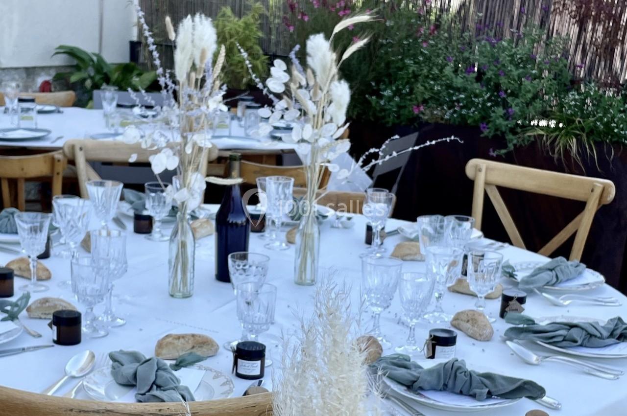 Table dressée en extérieur avec nappes blanches, vaisselle élégante, bouquets de fleurs séchées et décorations naturelles.