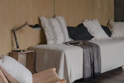 Canapé beige avec coussins blancs et noirs, plaid gris, lampe de bureau noire et table d'appoint en bois.