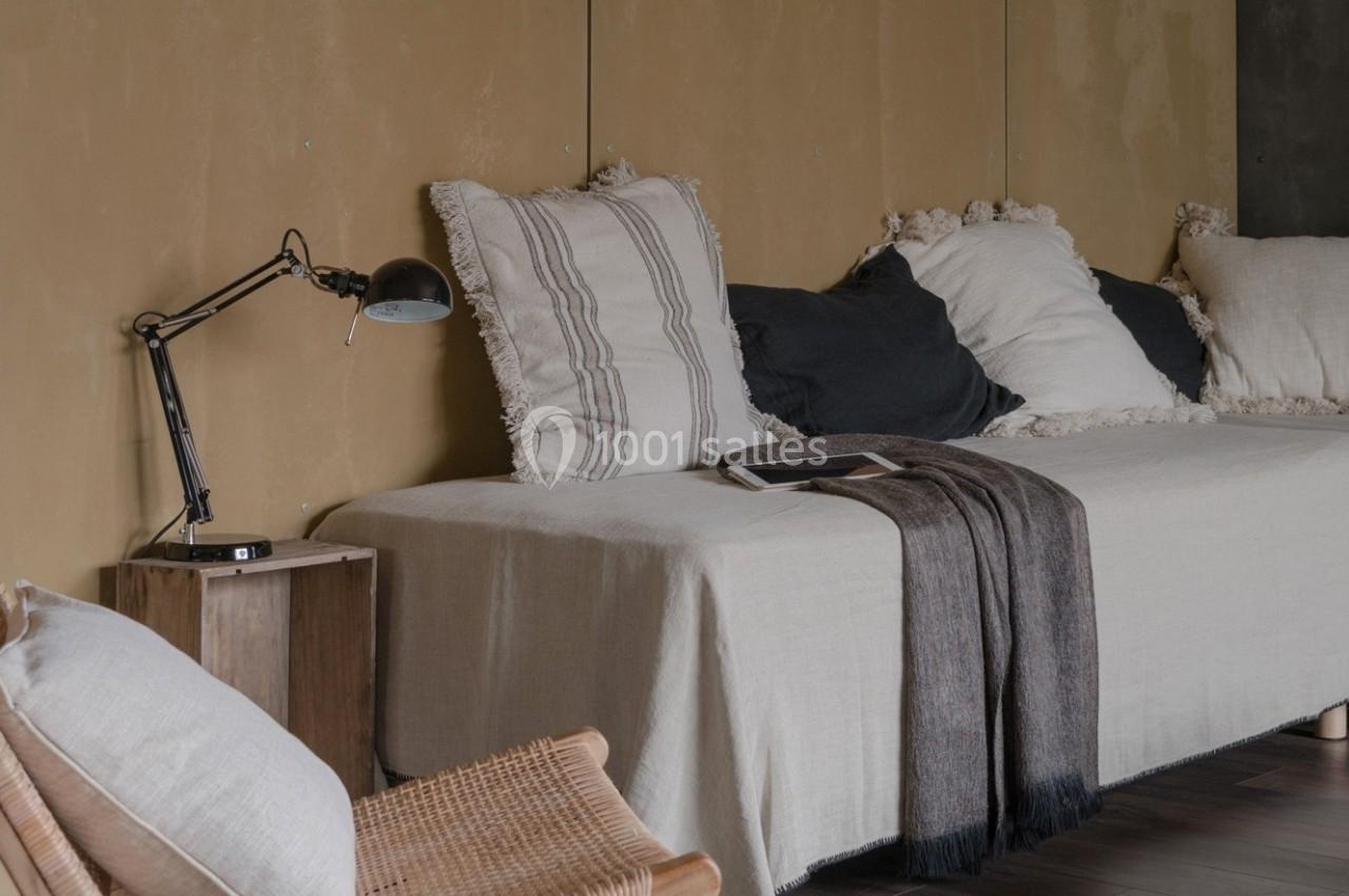 Canapé beige avec coussins blancs et noirs, lampe de bureau noire sur une table en bois, plaid sombre posé.