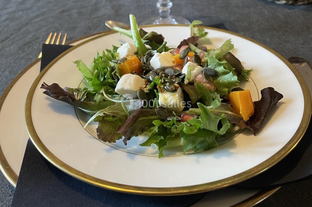 Assiette de salade composée avec feuilles vertes, cubes de fromage, morceaux de courge et graines, sur une table dressée.