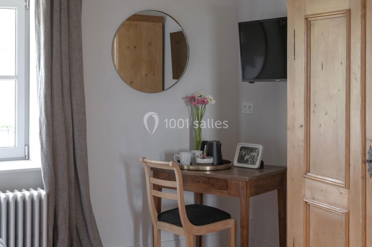 Coin bureau avec une table en bois, chaise, miroir rond, télévision murale, fleurs et une fenêtre avec rideau.