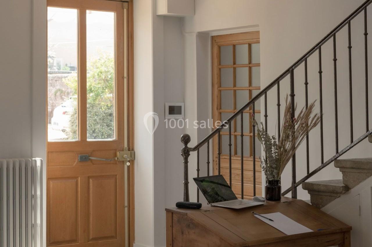 Entrée lumineuse avec porte en bois, escalier en métal, bureau en bois et ordinateur portable ouvert.
