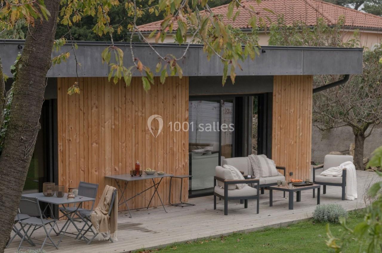 Terrasse en bois aménagée avec mobilier d'extérieur, adossée à une maison en bois et entourée de verdure.
