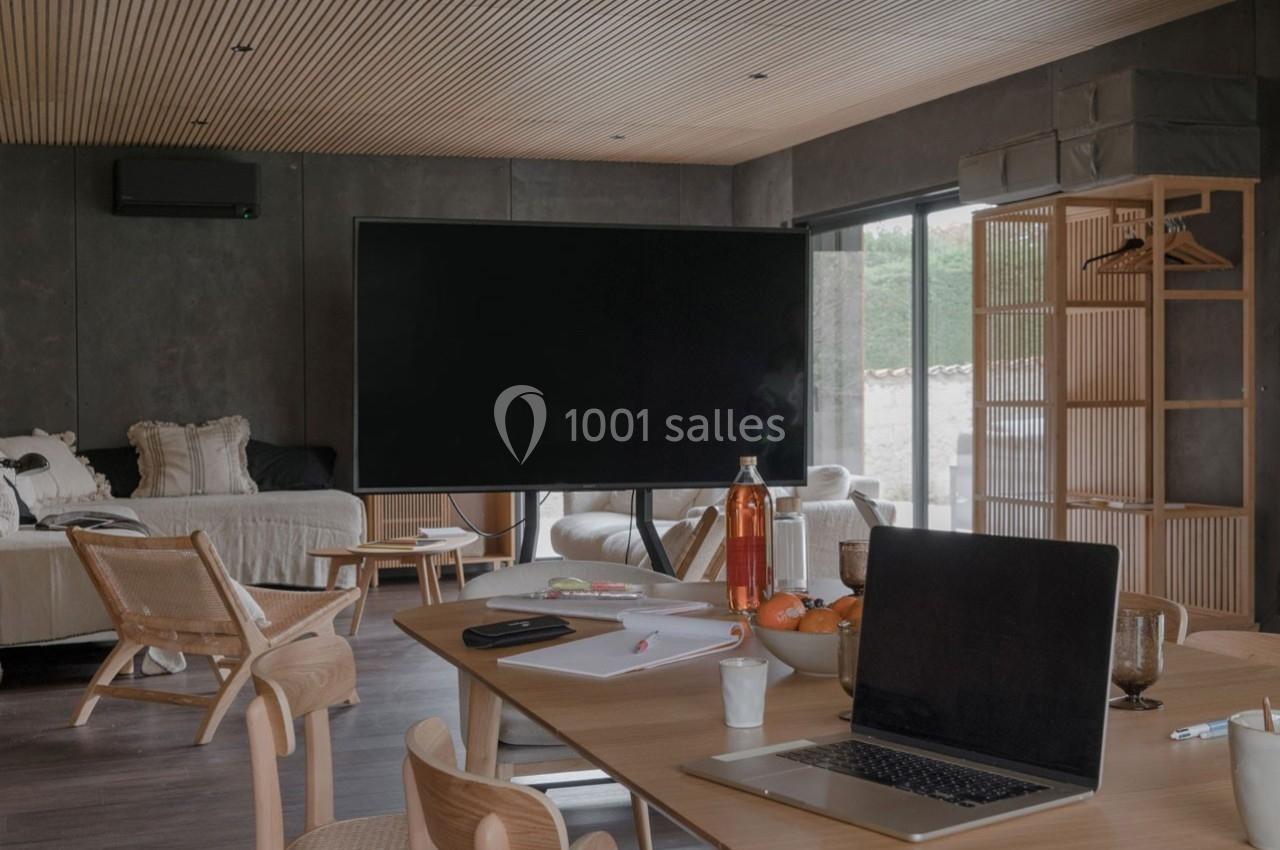 Salle de réunion moderne avec table en bois, ordinateur portable, écran noir et fauteuils en bois clair.