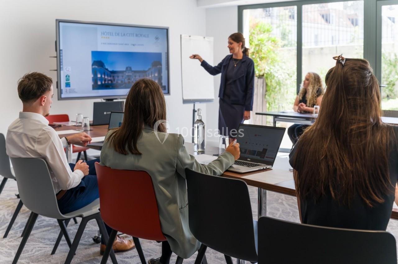Une réunion professionnelle avec une présentation sur écran dans une salle lumineuse équipée de grandes fenêtres.