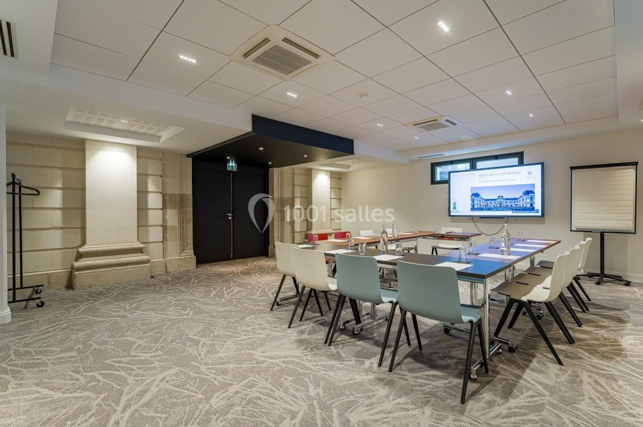 Salle de réunion lumineuse avec table rectangulaire, chaises modernes, écran, paperboard et décorations murales.